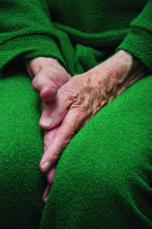 Old woman's hands tucked between her legs